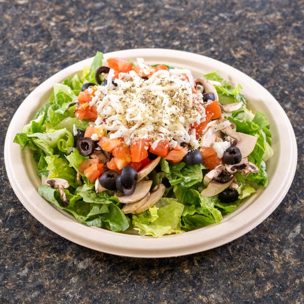 Fresh garden salad with lettuce, tomatoes, black olives, mushrooms, and shredded cheese in a bowl.