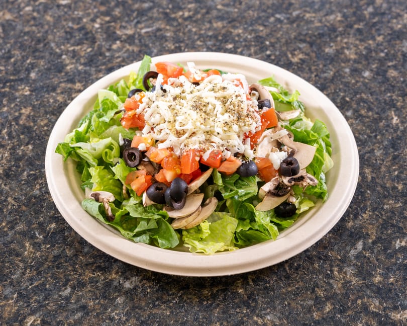 Fresh garden salad with lettuce, tomatoes, black olives, mushrooms, and shredded cheese in a bowl.