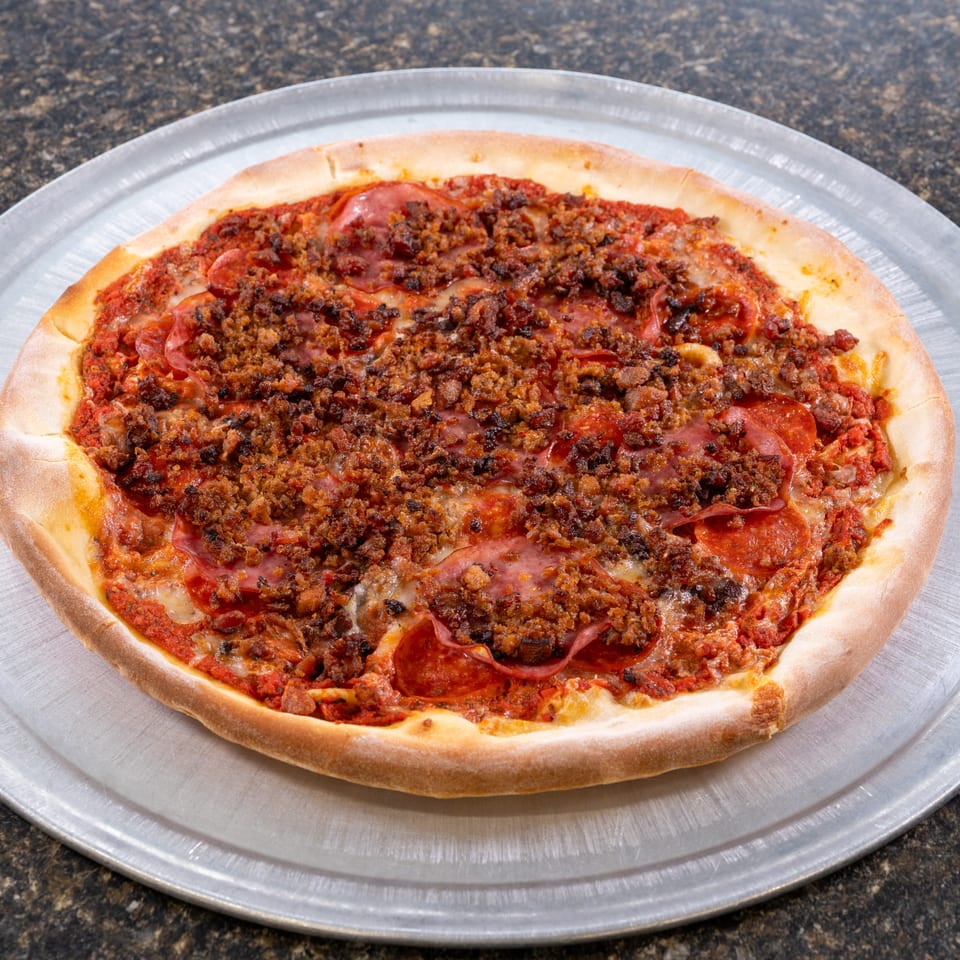 A whole meat lover's pizza with pepperoni and sausage on a metal pizza pan.