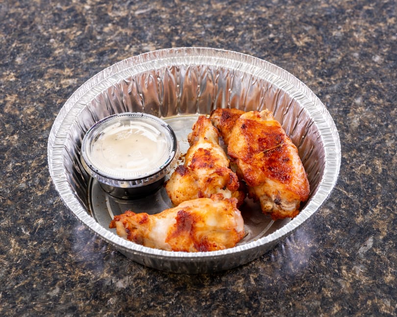 Three crispy chicken wings and a small cup of dipping sauce in a foil container.