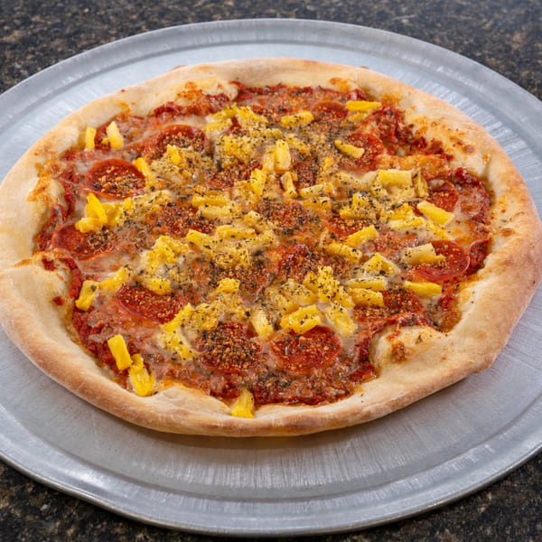 A whole pepperoni and pineapple pizza, topped with herbs, on a metal pizza pan.