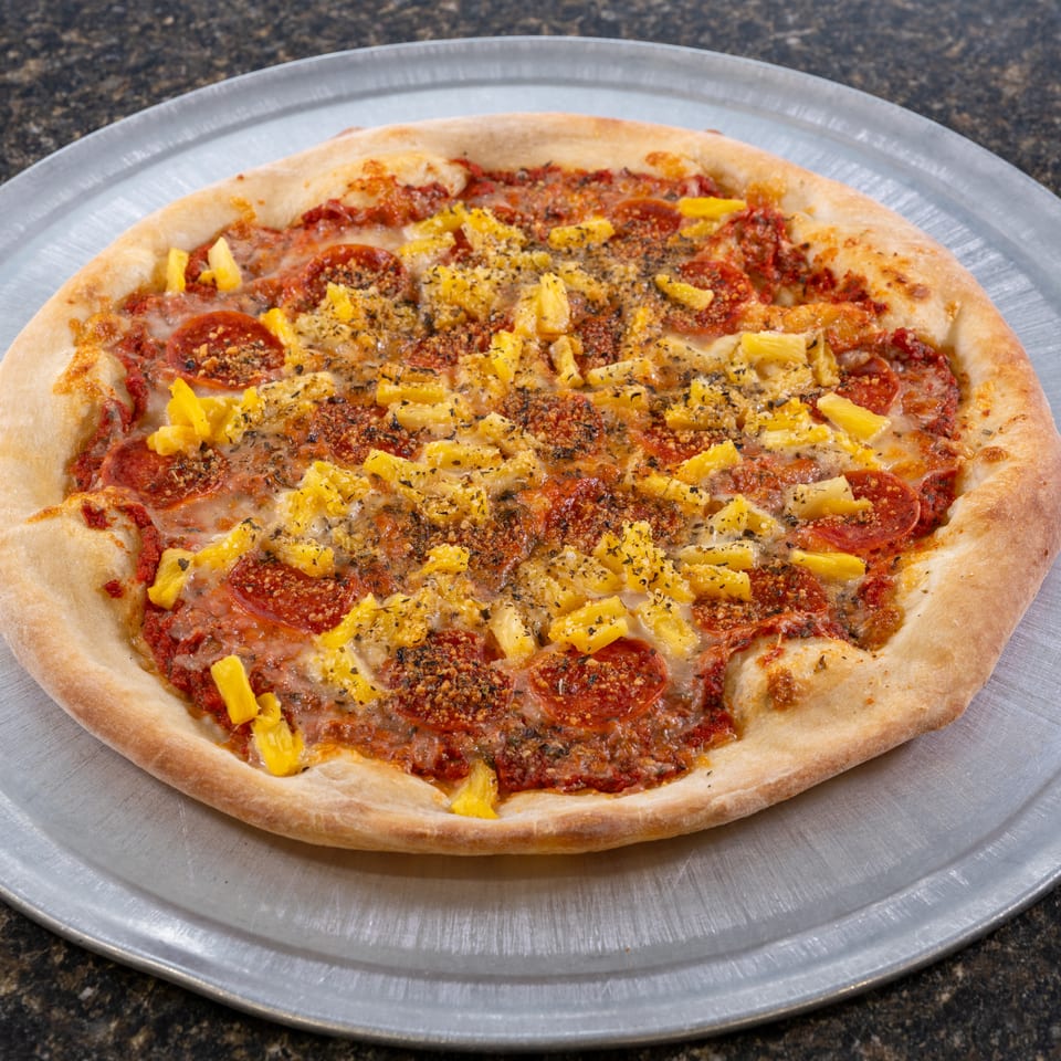 A whole pepperoni and pineapple pizza, topped with herbs, on a metal pizza pan.