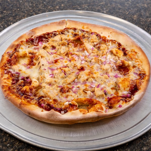 A BBQ chicken pizza with red onions and melted cheese on a metal pan.