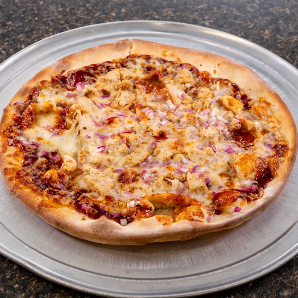 A BBQ chicken pizza with red onions and melted cheese on a metal pan.