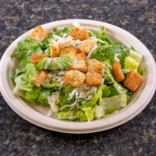 A Caesar salad with romaine lettuce, croutons, and shredded cheese in a beige bowl.