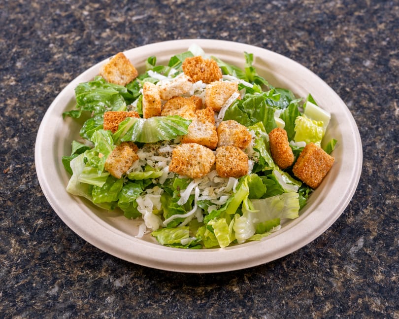 A Caesar salad with romaine lettuce, croutons, and shredded cheese in a beige bowl.