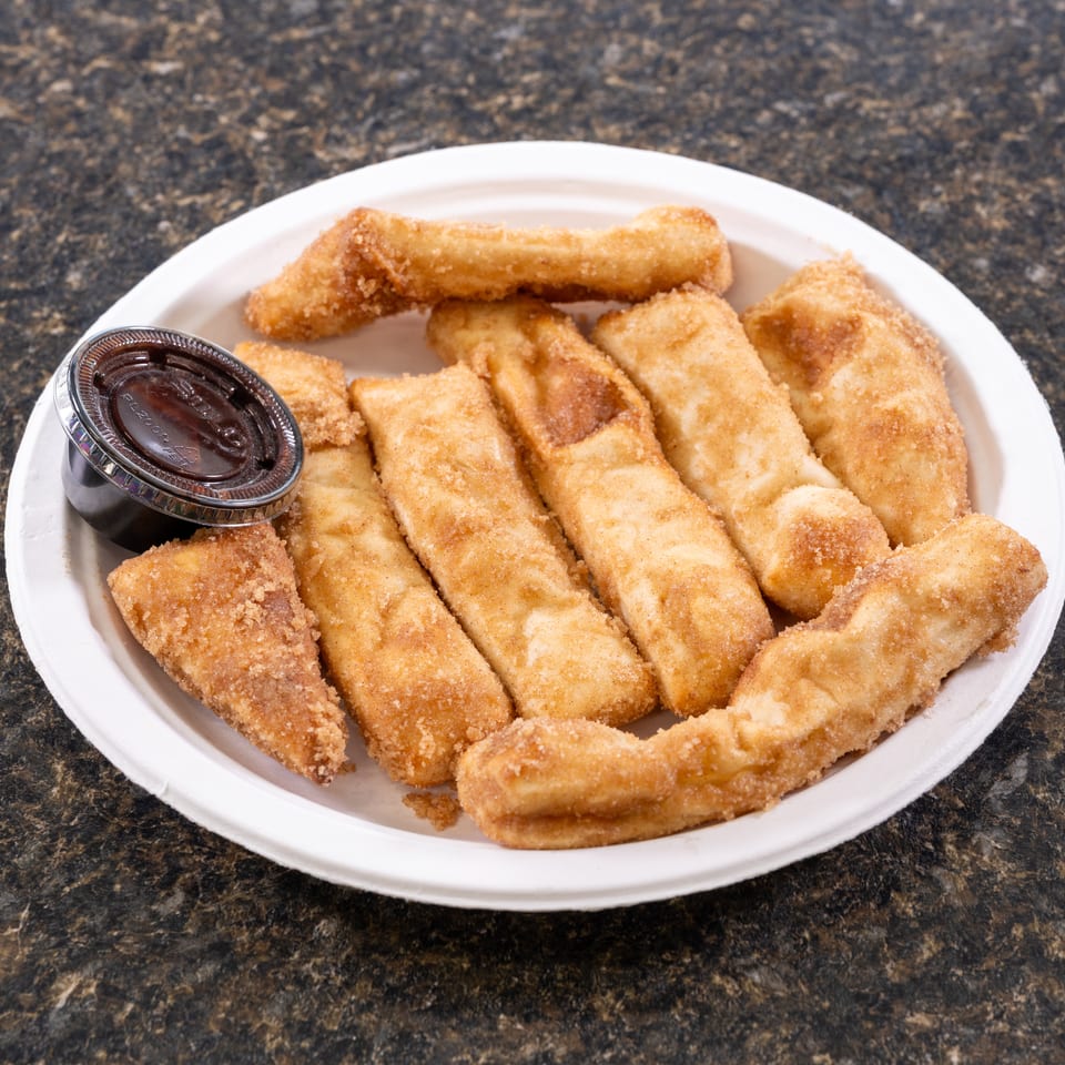 A white plate filled with golden-brown churro sticks and a small cup of chocolate dipping sauce.