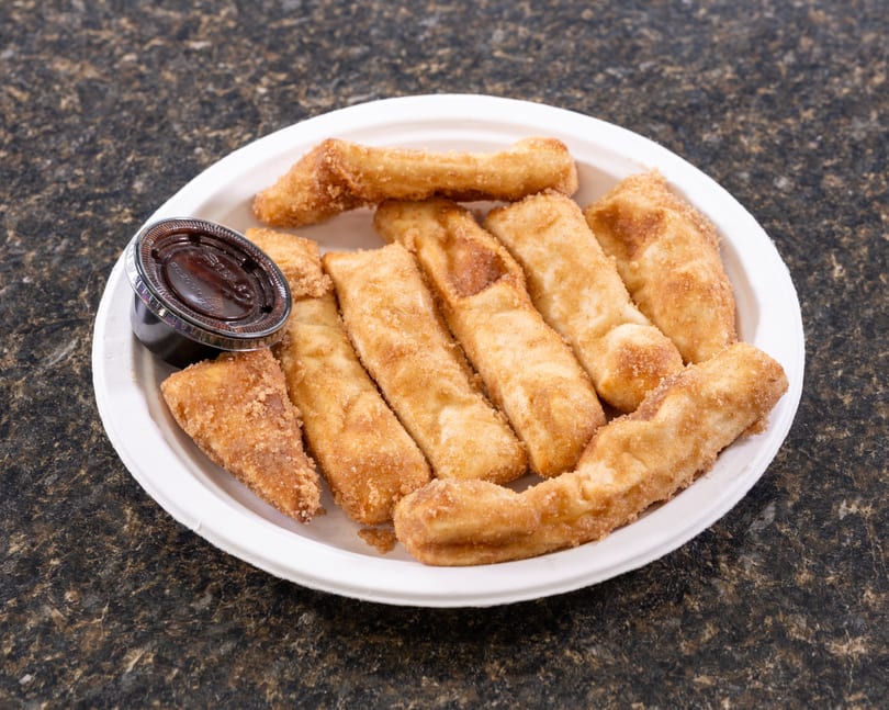 A white plate filled with golden-brown churro sticks and a small cup of chocolate dipping sauce.